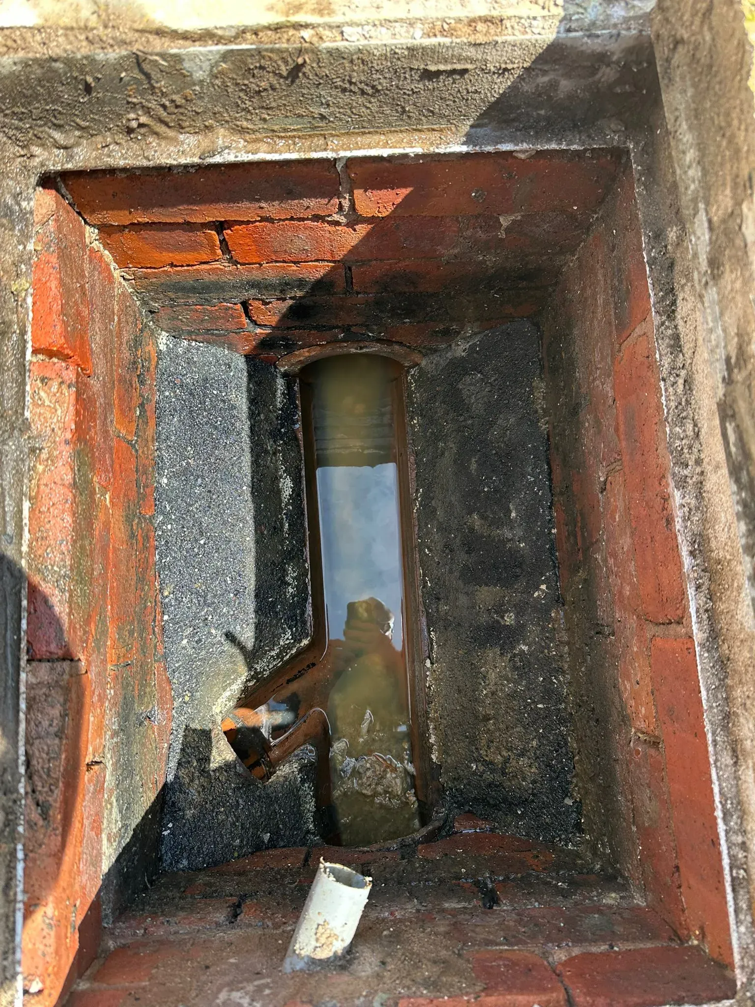 Blocked outdoor drain showing a water backup in a brick manhole.