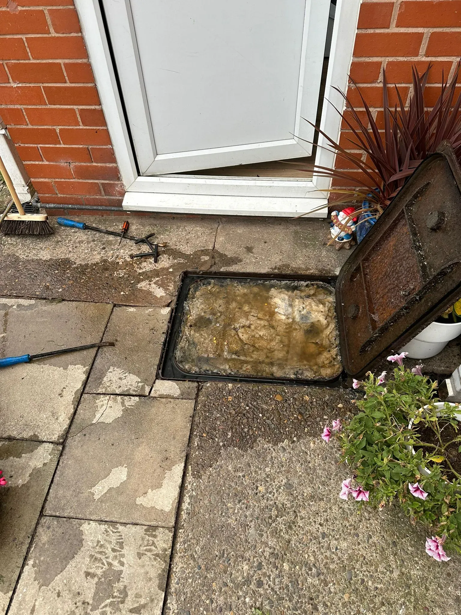 Severely blocked manhole overflowing with foul water and debris outside a residential home, indicating an urgent drainage problem.