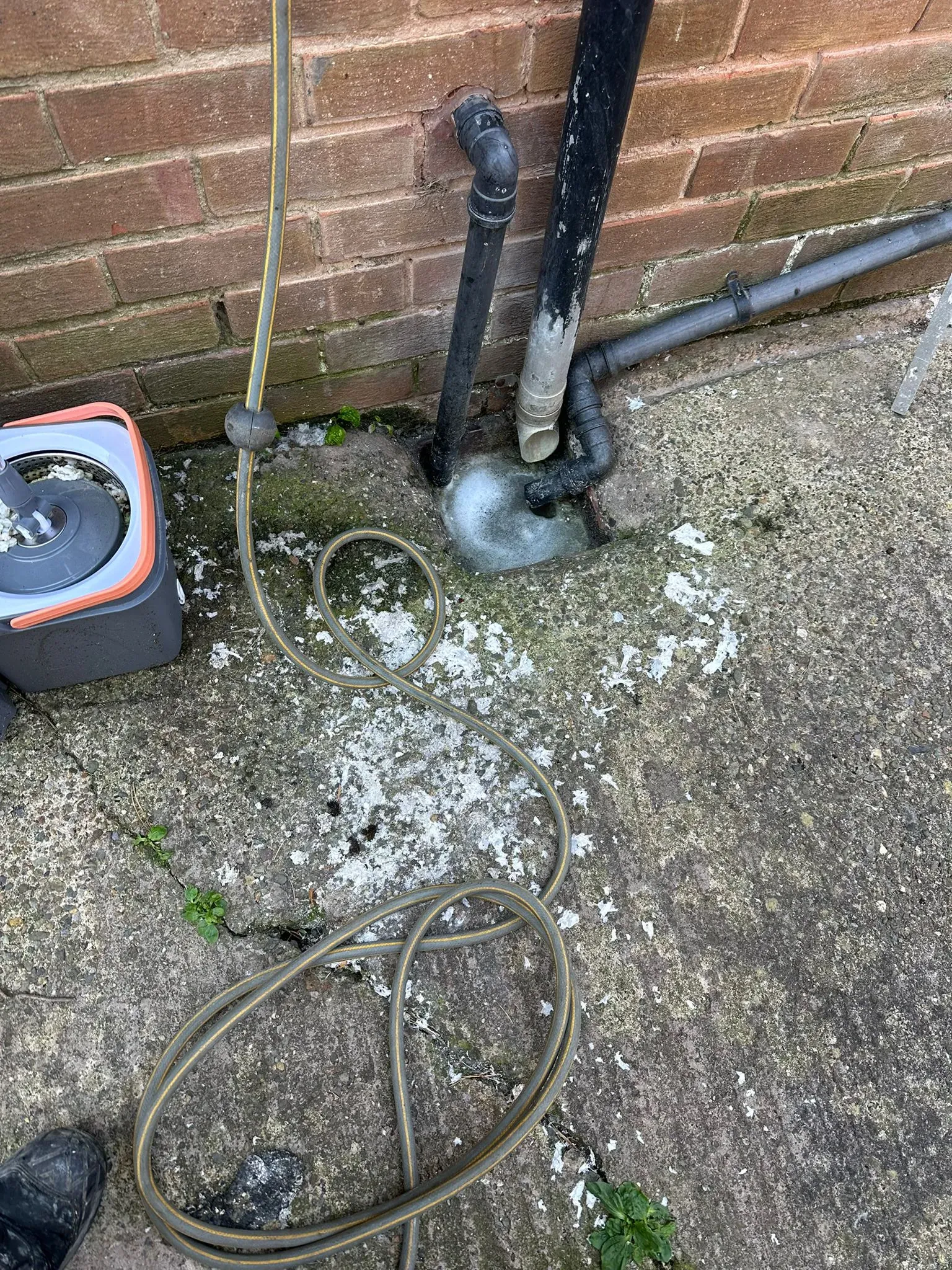A picture of an outdoor drain with white residue and a garden hose, indicating a drainage problem or recent cleaning.
