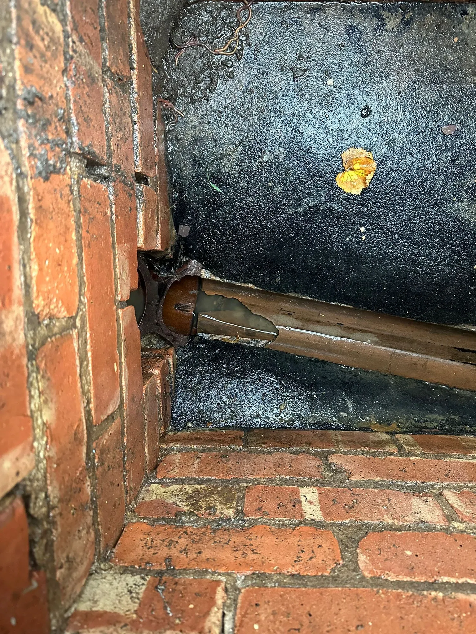 Damaged, cracked drain pipe with standing water inside a brick inspection chamber, highlighting a blocked drain.